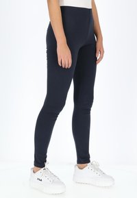 Marineblauwe ribgebreide leggings met een aansluitend ontwerp, vervaardigd uit rekbare stof. G gedragen met witte platform sneakers. Gladde, elastische tailleband.