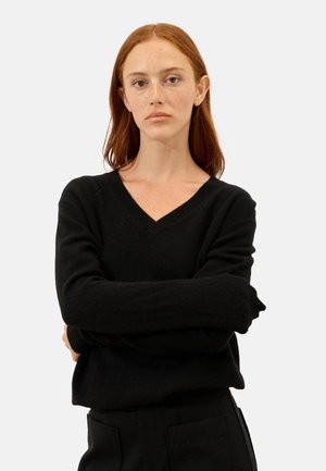 Czarny sweter z dekoltem w kształcie litery V, z długimi rękawami, wykonany z miękkiego materiału. Tekstura wydaje się gładka, ma luźny krój i minimalne detale.