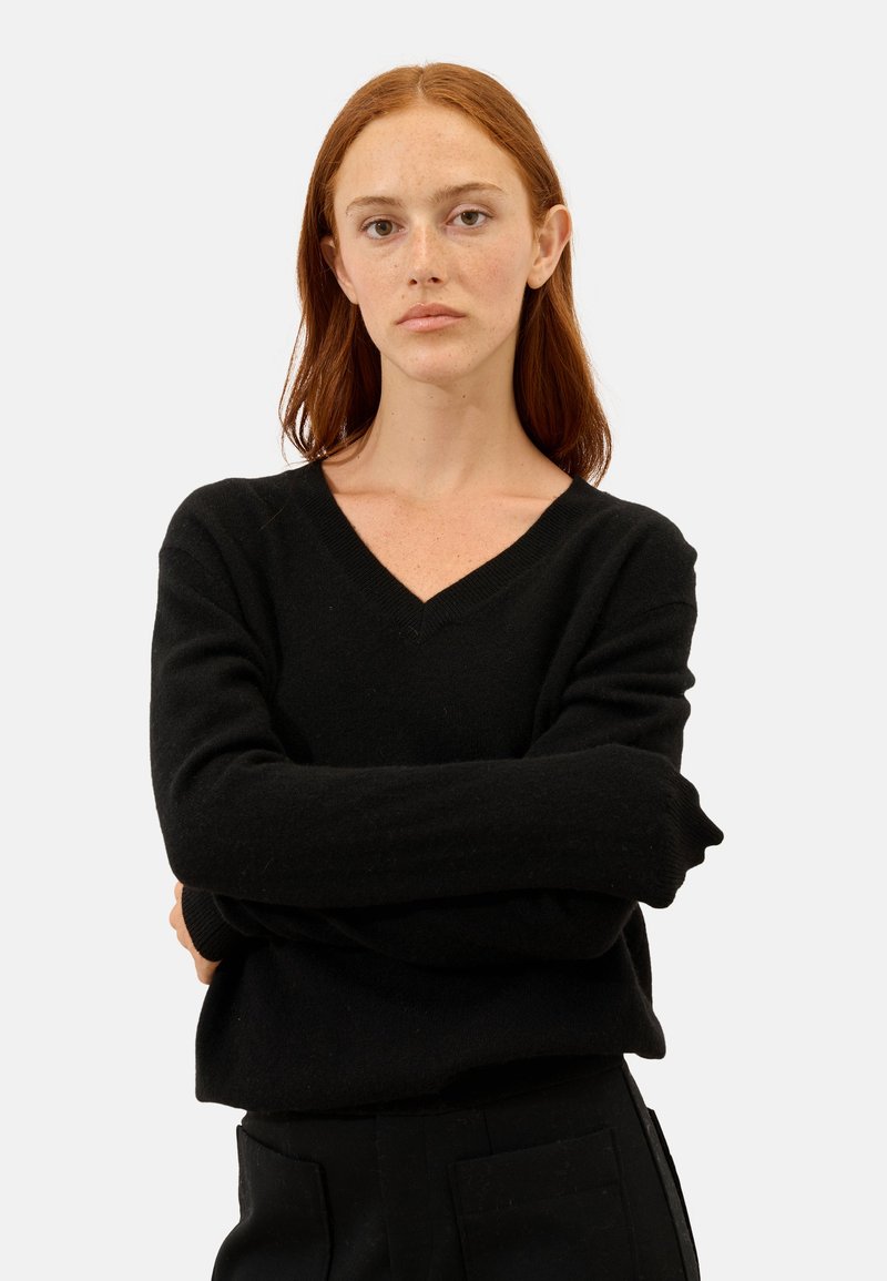 Schwarzer V-Ausschnitt-Pullover mit langen Ärmeln, aus weichem Stoff. Die Textur wirkt glatt, hat einen lockeren Schnitt und minimale Details.