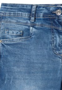 Jean en denim bleu avec une texture lisse, doté d'une petite poche avant et d'une poche arrière standard, fini avec des surpiqûres contrastantes jaunes.