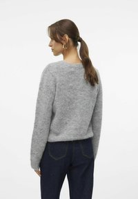 Pull en cachemire gris avec un col rond, des manches longues et une coupe décontractée, associé à un jean bleu foncé. Texture subtile, design minimaliste.