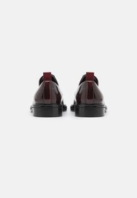 Chaussures en cuir verni bourgogne avec un bout rond et une semelle noire. Présentent une languette en tissu à l'arrière pour un enfilage facile.