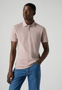 Ljusrosa polo skjorta gjord av mjukt material, har en krage, kort ärm och en subtil bröstlogo. Matchad med blå jeans.