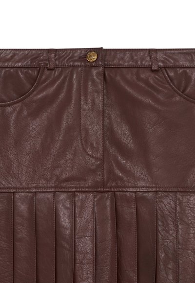 Bruine leren rok met plooien aan de onderkant, voorzien van een knoopsluiting en zakken. Gladde textuur met een lichte glans.
