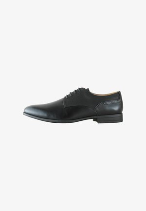 Schwarzer Herrenschuh mit Schnürverschluss, glatter Zehenpartie, strukturierten Seitenpaneelen und niedrigem gestapeltem Absatz, seitlich auf weißem Hintergrund gezeigt.