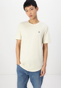 Lichtbeige t-shirt met korte mouwen en een ronde halslijn, voorzien van een klein zwart logo op de linkerborst. Zachte stof en een ontspannen pasvorm.