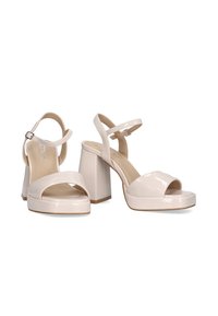 Sandalias de tacón block de charol beige con punta abierta, correa ajustable en el tobillo y textura suave. El diseño sutil de la plataforma realza la altura.