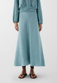 Gonna maxi lunga di un blu chiaro, realizzata in un tessuto testurizzato, caratterizzata da una vita aderente e un design fluido. Abbinate a sandali neri piatti.