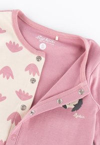 Pink cotton onesie with a beige side featuring pink leaf patterns, snap buttons, and a graphic of a bear face. Label reads "sigikid."
