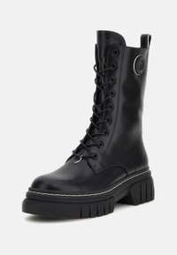 Stivale da combattimento nero con lacci, realizzato in pelle liscia, con suola in gomma spessa, cuciture bianche e un logo circolare sulla parte superiore.