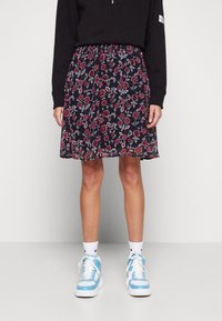 Blommig kjol i marinblått med röd och vit blomsterämn; lättviktsmaterial; elastisk midja; ihopparat med blå sneakers och vita strumpor.