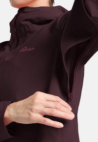 Bordeaux waterproof jack met een ritssluitingventilatie, voorzien van een hoge kraag en een geborduurd logo. Glad textuur met verstelbare koordjes.