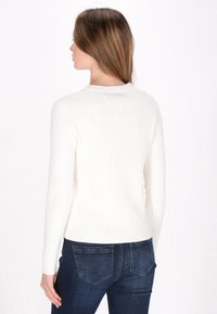 Witte kabelgebreide trui met geribbelde halslijn en manchetten, aansluitend ontwerp. Gepaarde met donkerblauwe jeans met gebogen stiksel op de achterzak.