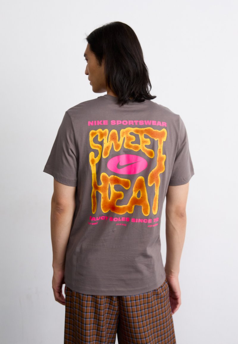 Sivi pamučni majica s velikim šarenim tekstom na leđima koji glasi "SWEET HEAT" u žutoj i ružičastoj boji, logo ispod, kratki rukavi, ravnog kroja.