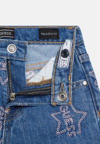 Jeansy palazzo z denimu w jasnym niebieskim kolorze z złotym przeszyciem, srebrnymi elementami metalowymi oraz haftem w kształcie gwiazdek na przednich kieszeniach.