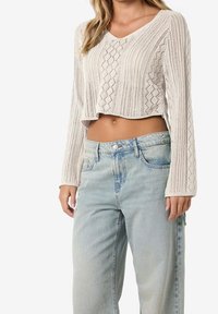 Virkat, långärmad, krämfärgad topp med V-hals, croppad design och öppen diamantmönster; paired med ljusblå, löst sittande jeans.