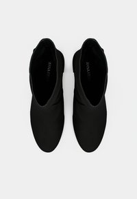 Μαύρα μποτάκια αστραγάλου με λεία υφή και στρογγυλεμένη μύτη, με μίνιμαλ σχεδιασμό και ευέλικτο επάνω μέρος. Η ετικέτα στο εσωτερικό γράφει "ANNA FIELD."