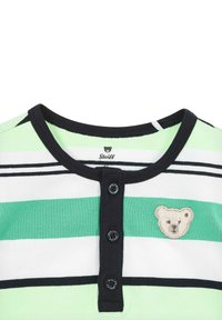 Camisa de manga corta a rayas en verde, blanco y negro, con un cuello azul marino. Presenta una tapeta con botones y un parche de oso en el lado izquierdo del pecho.