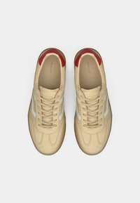 Baskets beiges avec des bandes latérales blanches et des accents rouges. Matériau supérieur lisse, bout arrondi et design traditionnel à lacets.