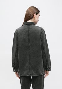 Temno siva denim jakna z oblikovano silhueto, gumbi na manšetah in vidnimi šivi; ovratnik in dolgi rokavi.