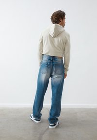 Light gray cropped hoodie with a drawstring hood, paired with faded blue denim jeans featuring a loose fit and a slight flare.