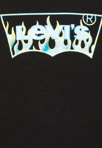 Svart t-shirt med en Levi's-logotyp i reflekterande blå och gula lågflammande, centrerad på bröstet, med mjuk textur och avslappnad design.