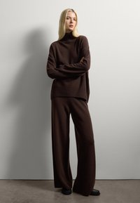 Dark brown knitted sweater with a high neck and ribbed hem, paired with matching wide-leg trousers. Smooth texture and relaxed fit.