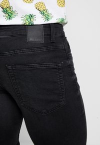 Jeans de denim negro con un diseño ajustado, bolsillos planos y una etiqueta con marca en relieve en la parte trasera de la cintura.