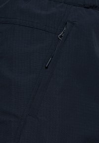 Ciemna tkanina z ukośną kieszenią na zamek błyskawiczny, wyposażona w czarny suwak i subtelne przeszycia z wzorem w kratę.