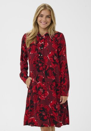 Rød kjole med lange ærmer og blomstermønster i nuancer af rød og sort. Har en krave, knapdetaljer og sidelommer.