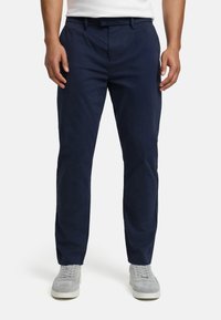 Pantaloni di cotone blu navy con taglio dritto, passanti per cintura e tasche frontali, abbinati a sneakers grigio chiaro.