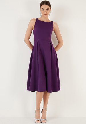 Purple sleeveless dress with a fitted bodice, flared skirt, and pleats; made from smooth fabric. Paired with silver strappy heels.