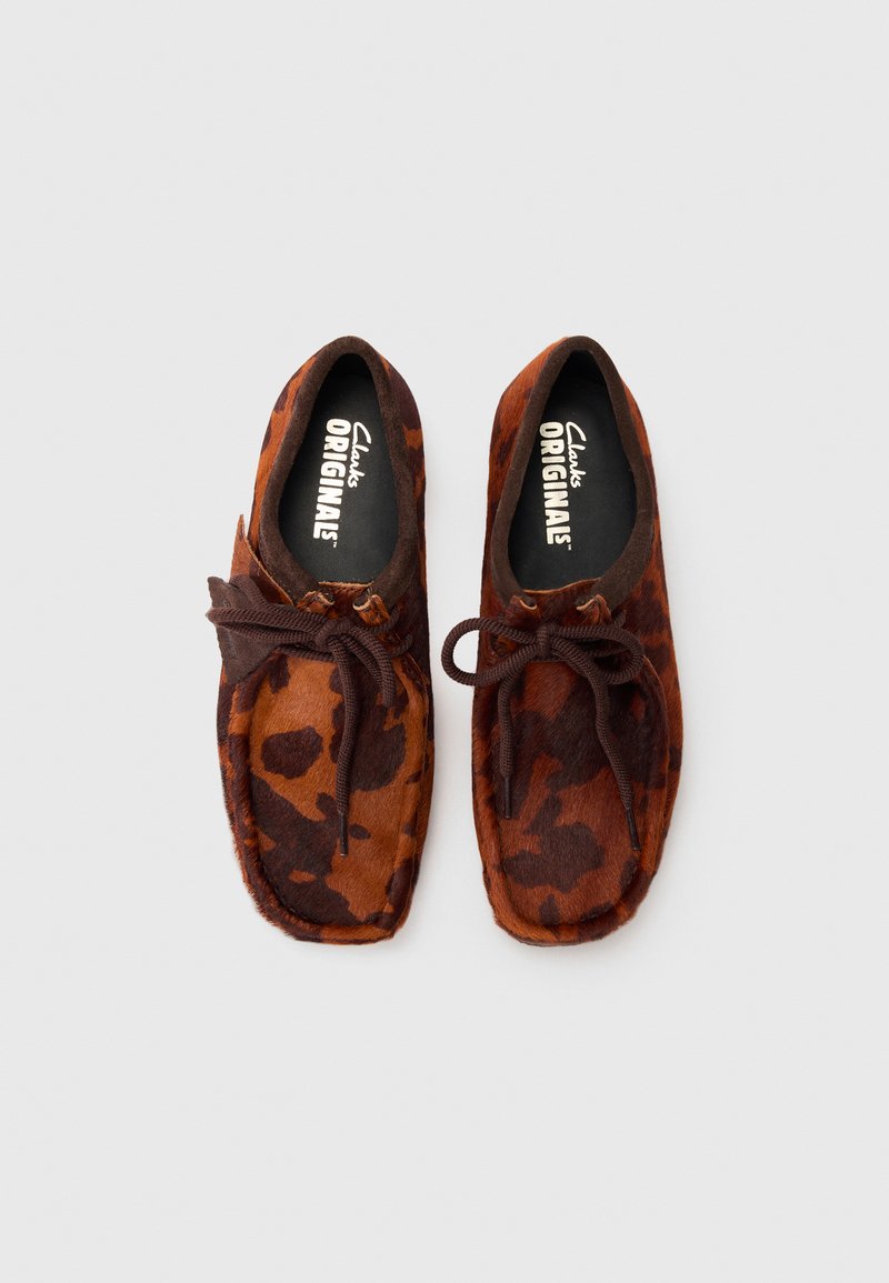 Braune und beigefarbene Slip-On-Schuhe mit Muster aus weichem Wildleder, rundem Zeh, Schnürverschluss und strukturierten Akzenten.