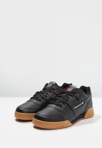 Sorte lær sneakers med lavt design, som har en teksturert svart tunge, perforert tåboks og en gummigummi såle. Røde og hvite detaljer.
