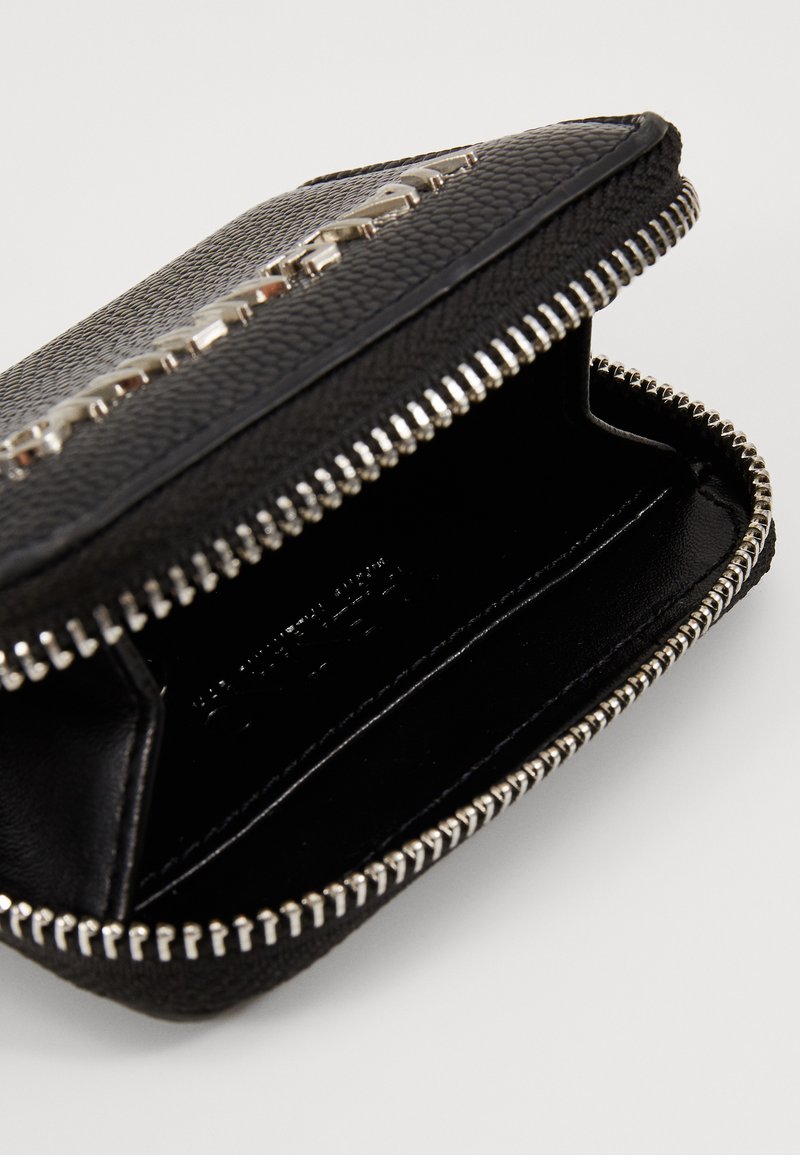 Cartera de cuero negra con exterior texturizado, cierre de cremallera plateado y herrajes brillantes. El interior es de tela negra suave sin compartimentos visibles.