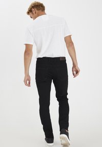 Zwarte denim jeans met een slim fit, vijf-pocket ontwerp en een leren tailleband patch. Draagt een wit shirt met korte mouwen en donkere schoenen.
