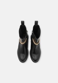 Czarne skórzane botki za kostkę z złotym łańcuchem z przodu i pętlami do zakupu z tyłu, zaprezentowane z widoku z góry.