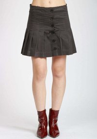 Gonna plissettata grigia con vita alta, chiusura frontale con bottoni scuri e tessuto strutturato. Abbinata a stivaletti rossi lucidi.