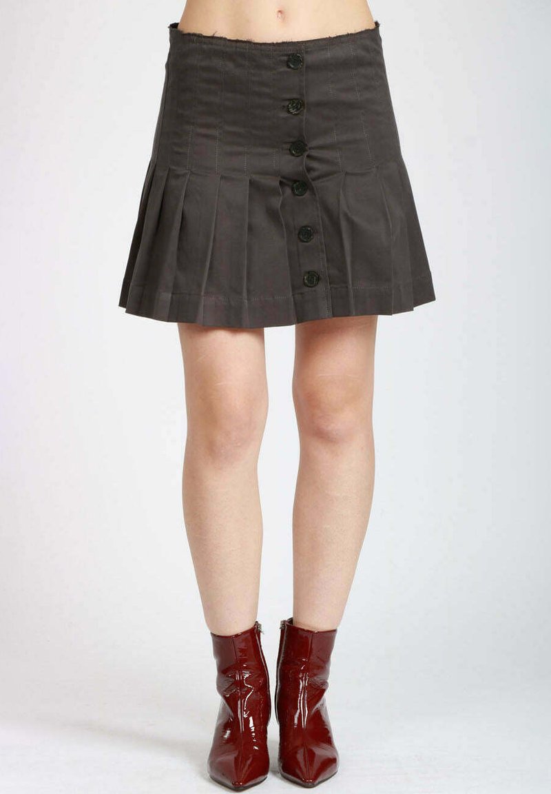 Gonna plissettata grigia con vita alta, chiusura frontale con bottoni scuri e tessuto strutturato. Abbinata a stivaletti rossi lucidi.