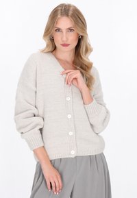 Jasnoszary sweter robiony na drutach z dekoltem w serek, zoversized rękawami i pięcioma białymi guzikami z przodu. Teksturowana tkanina z ściągaczami przy mankietach.
