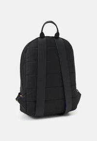 Zaino nero con una texture trapuntata, forma arrotondata elegante, spallacci imbottiti e una maniglia superiore per il trasporto.