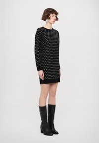 Abito lavorato a maglia nero con motivo a pois argento, maniche lunghe e scollatura rotonda, abbinato a stivali neri con tacco al ginocchio.
