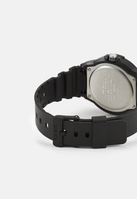 Montre Casio noire avec un bracelet en caoutchouc texturé, un dos métallique, cinq trous d'ajustement et un boîtier argenté. Design simple et fonctionnalité.