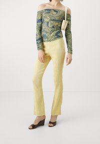 Off-shoulder top with blue and yellow abstract pattern; light yellow textured pants; brown wedge sandals; small white bag with shoulder strap.