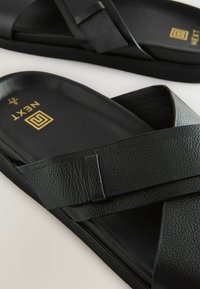 Sandales noires à glissière avec un dessus en synthétique texturé et une semelle lisse. Présentent des sangles entrecroisées et un logo doré en détail sur la semelle intérieure.