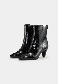Botas negras hasta el tobillo con una textura brillante en patrón de cocodrilo, punteras afiladas y un tacón de altura media; cremallera lateral para facilitar su uso.