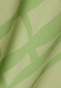 Tejido de punto en verde claro con patrones geométricos en verde más oscuro y superficie texturizada, mostrando diferentes tonos y líneas.