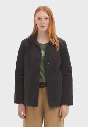 Giacca in corduroy grigio scuro con colletto, bottoni frontali e due tasche, indossata sopra una camicia verde. Tessuto liscio con motivo a coste.