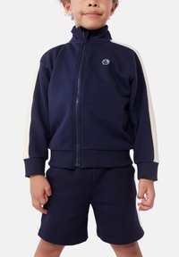 Marineblauer Trainingsanzug mit weißen Seitenstreifen; Reißverschlussjacke mit hohem Kragen, gerippten Bündchen und passender Shorts, aus weichem Stoff gefertigt.