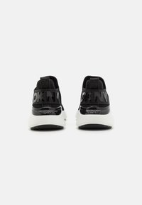 Sneakers neri con tomaia in rete, dettagli lucidi in vernice e il logo audace "DKNY" sul tallone. Sole bianco spesso per un contrasto.
